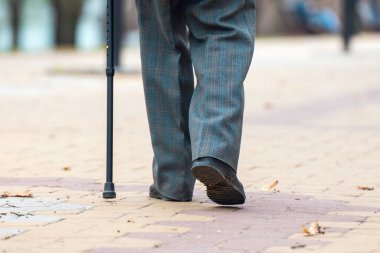Legs of an elderly man walking with a cane on the street. clipart