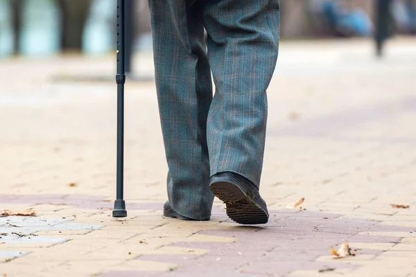 Legs of an elderly man walking with a cane on the street.