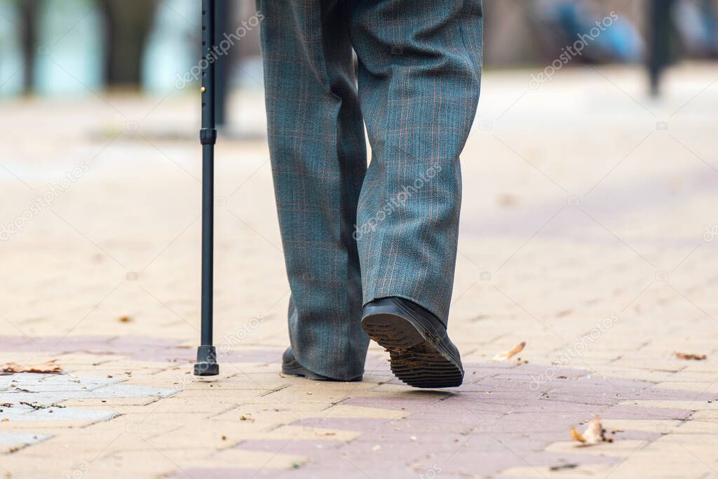 Legs of an elderly man walking with a cane on the street.
