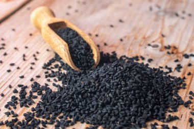 Siyah kimyon tohumları ve ahşap kepçe, doku arka planı.