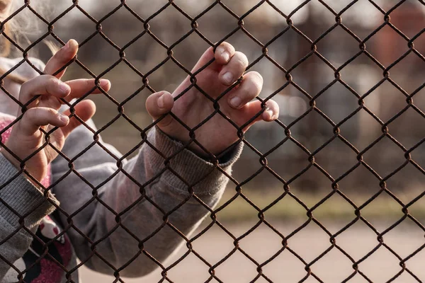 The child\'s hands are holding onto a metal mesh fence. Social problem of refugees and forced migrants.