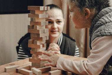 Anne ve kızı tahta bloklardan bir kule inşa etmek için masa oyunu oynuyorlar..