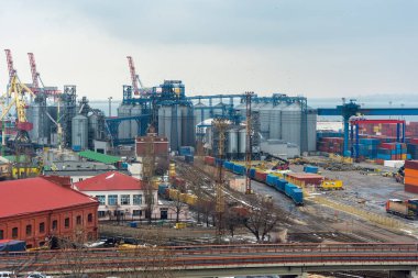 Stacked cargo containers and grain storage in cargo seaport storage area on cloudy day.