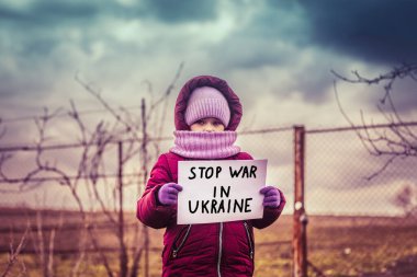 Üzgün bakışlı küçük mülteci kız ve Ukrayna 'daki savaşı durdurun yazan bir afiş. Mültecilerin ve yerlerinden edilen insanların sosyal sorunları. Rusya 'nın Ukrayna halkına karşı savaşı.