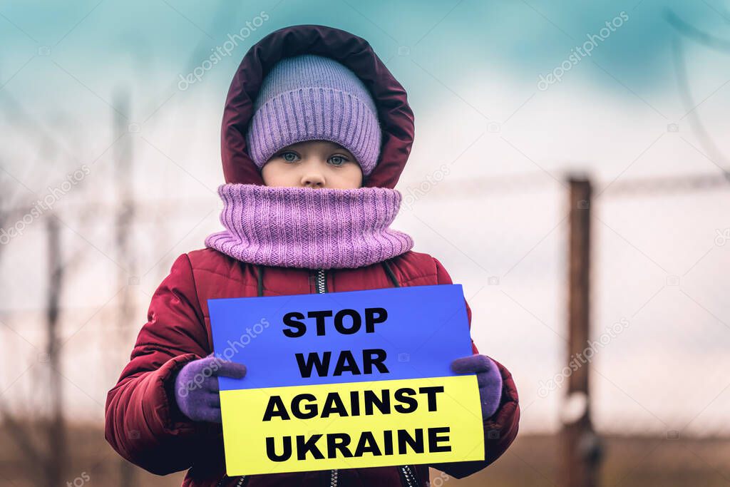 A little refugee girl with a sad look on her face and a Ukrainian flag that says stop war against Ukraine. The social problem of refugees and displaced persons. Russia's war against the Ukrainian people.