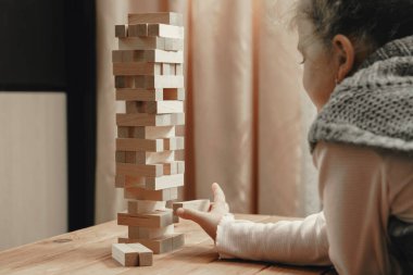 Masa oyunu oynayan şirin küçük kız, tahta bloklardan kule inşa ediyor..
