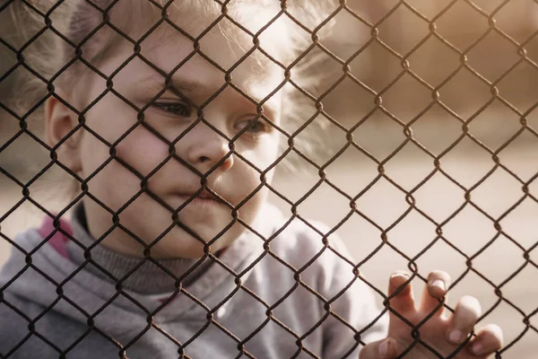 金属製の柵の後ろに悲しい表情をした少女 ロシア占領地へのウクライナの子供の強制送還の問題 — ストック写真
