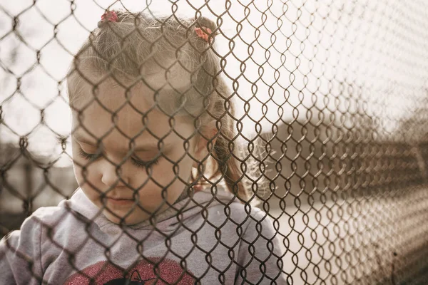 金属製の柵の後ろに悲しい表情をした少女 ロシア占領地へのウクライナの子供の強制送還の問題 — ストック写真