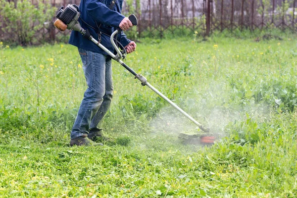 The gardener mows the grass with a trimmer in the garden.
