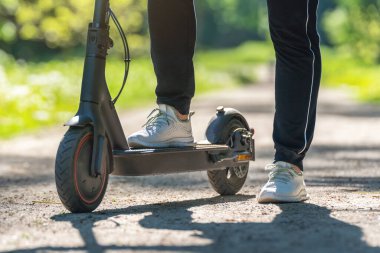 Parktaki toprak yolda elektrikli scooter kullanan genç bir kadın..