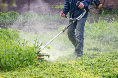 Bahçıvan bahçede bir budama makinesiyle çimleri biçer..
