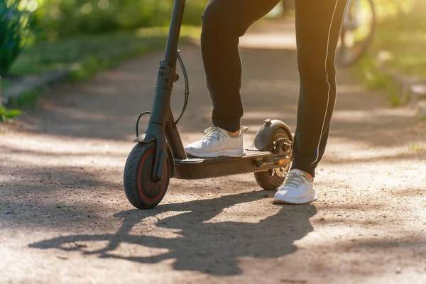 Young woman on an electric scooter on a dirt road in the park.