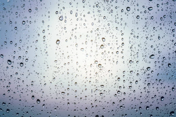 Raindrops on window glass, cloudy weather, background texture