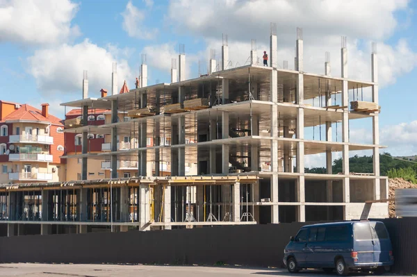 A residential and office building is under construction. The concrete frame of the future multi-storey residential building and office premises, against the background of a blue sky with white clouds.