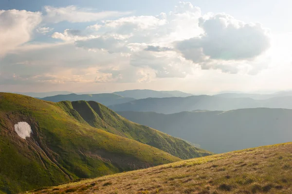 The diverse relief of the Carpathian Mountains with a white spot of snow that has not yet fully melted and a smoky horizon against the background of a gray sky with clouds
