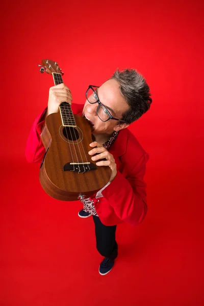 high angle plane of a musician biting his ukulele funny expression. Isolated on red background