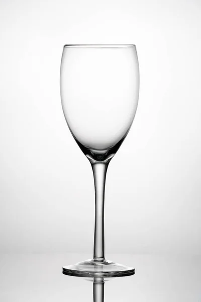 Empty wine glass on reflective surface. White background with gray vignette