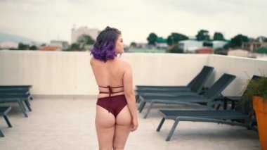 curvy girl walking away from the camera, she turns and places her hands on her waist, with short dyed hair fluttering in the wind. Slow motion