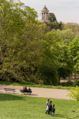 Park des Buttes Chaumont. Belvedere Adası 'ndaki Sibyl Tapınağı manzarası ve yürüyen ve oturan insanlar.