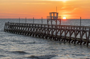 View of a wooden pier in front of the sea, a colorful sunrise and Le Havre city buildings far away