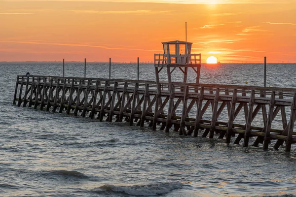 View of a wooden pier in front of the sea, a colorful sunrise and Le Havre city buildings far away