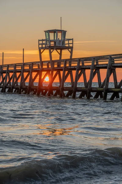 View of a wooden pier in front of the sea, a colorful sunrise and Le Havre city buildings far away