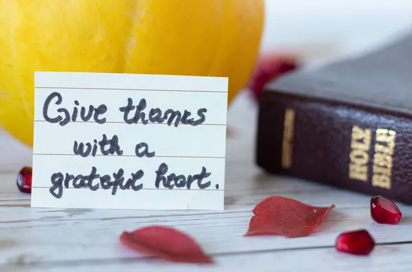 Give thanks with a grateful heart, a handwritten quote with Holy Bible Book, pumpkin, pomegranate seeds, and red leaves. The biblical concept of thanksgiving to God Jesus Christ. A closeup.