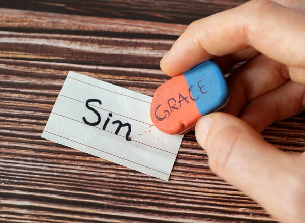 A handwritten word sin with a hand holding a rubber eraser with grace text on wooden background. Christian biblical concept of grace, mercy, sacrifice, and sacrifice of God Jesus Christ. A close-up.