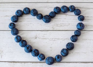 Tahta bir masada kalp şeklinde dizilmiş taze yaban mersini. Üst Manzara. Mavi-mor renkli organik meyveler.