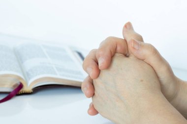 Kadınların elleri beyaz arka planda açık İncil kitabıyla dua ediyor. - Yakın çekim. İncil 'deki Hristiyan duası, inancı ve Tanrı' ya ve İsa 'ya olan güveni..