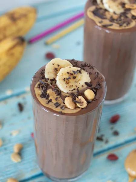 Fıstık ezmeli çikolatalı muzlu smoothie mavi ahşap bir masada bir bardakta. Seçici odaklanma. Yakın çekim..