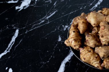 Karanlık bir granit masada izole edilmiş bir kasede, Kudüs enginar kökü sebzesi. Üst Manzara. Uzayı kopyala Yakın çekim..