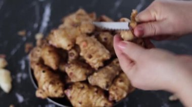 Kadının el ele tutuşması ve organik Kudüs enginarını mutfak bıçağıyla soyması ve arka planda bir kase çiğ güneş boğması. Sağlıklı bitki temelli kök sebze yeme kavramı. Yakın çekim..