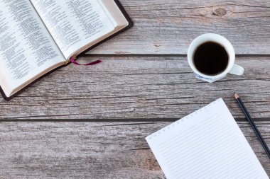 Kutsal Kitap 'ı boş bir defter, bir fincan kahve ve tahta bir masanın üzerindeki kalemle aç. Üst Manzara. Uzayı kopyala İncil 'deki İncil kavramı, Tanrı' dan esinlenilmiş kutsal kitaplardan alınmıştır..