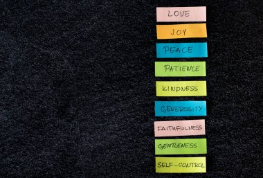 Colorful list of the fruits of the Holy Spirit (love, joy, peace, patience, kindness) isolated on dark background with copy space. Top view, a close-up. Christian fruit from Galatians Bible Book. clipart