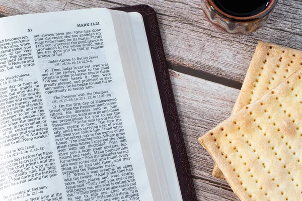 Unleavened bread, cup of wine, and open Holy Bible Book on wooden table. A close-up. Christian symbol of blood and body of the LORD Jesus Christ as a sacrifice for sins. Passover Holy Day celebration.