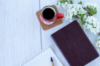Kapalı kutsal kitap, bir fincan kahve, çizgili defter ve fotokopi alanı olan çiçekler. Üst Manzara. Sabah Hıristiyan İncili dersi. Yakın çekim..
