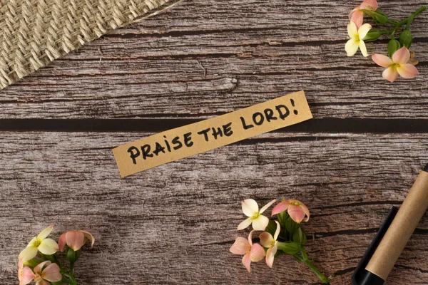 Praise the LORD, handwritten message quote from Christian Holy Bible on a wooden retro background with flowers in vintage style. Top view. Worship God Jesus Christ biblical concept. Flat lay.