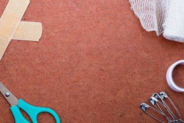 Arka plandaki ilk yardım seti parçaları: bandaj, tıbbi gazlı bez, makas, çengelli iğne ve dokumasız bant. Uzayı metin için kopyala. Üst manzara, düz yatış. Seyahat konseptinde acil yardım.