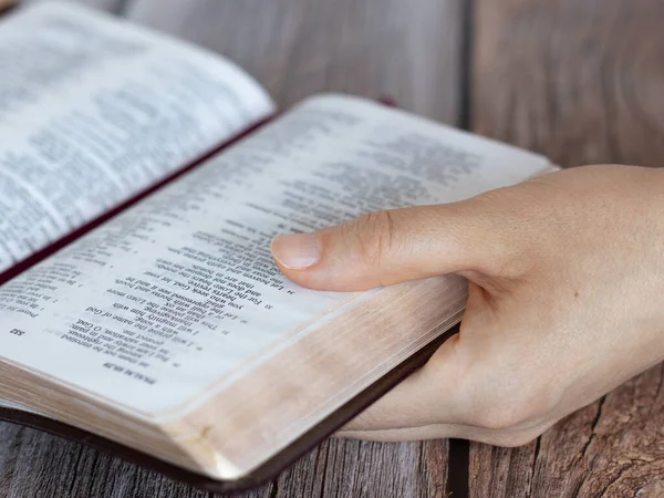 Female hand holding an open Holy Bible Book with golden pages. A closeup. Reading and studying Scriptures, Christian education, biblical concept.