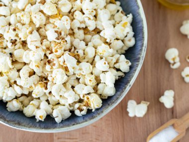 Kâsede ev yapımı patlamış mısır, tuzlu ahşap kaşık ve masada zeytinyağı. Üst manzara, yakın çekim. Tuzlu ve sağlıklı vejetaryen atıştırmalıkları. Düz yatıyordu.