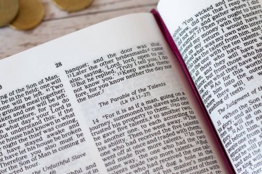 Kutsal Kitap 'ta yazılmış ve tahta bir masanın üzerinde birkaç altın sikke bulunan yetenekler misali. - Yakın çekim. Hıristiyan İncili kavramı.
