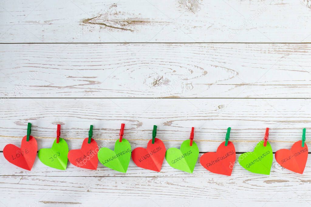 Paper hearts in red and green color with colorful clothespin hanging on a rustic line with biblical words: love, joy, peace. Fruits of the Spirit, Christian concept, Galatians 5. Top view. Copy space.