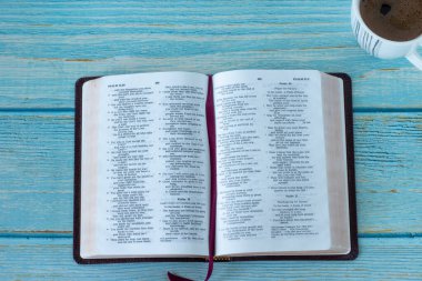 Open Holy Bible Book with a cup of coffee on a blue wooden background. Top table view, a closeup. Prayer, reading, and studying Christian Scriptures in the morning.