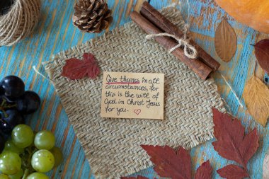 Handwritten message to give thanks to God Jesus Christ on a note in a vintage autumn setting with grapes, pumpkin, and dry leaves. Christian thanksgiving, gratitude, and praise concept. clipart
