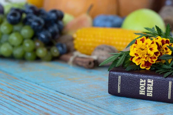 A closeup of a closed Holy Bible Book with flowers and fresh autumn food in the background. Thanksgiving day, Christian gratitude, blessing, and praise concept.