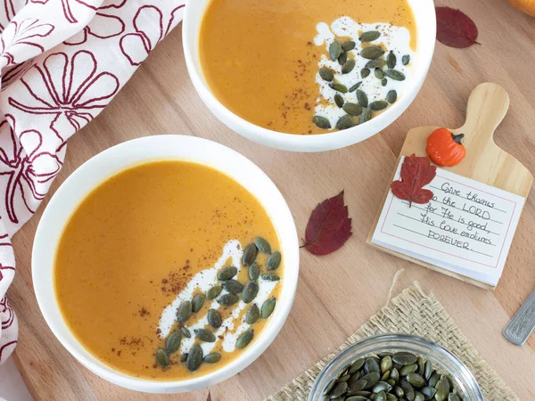 Vegan butternut squash soup in a bowl with coconut milk and pumpkin seeds on a wooden table with a handwritten note to praise and give thanks to the LORD. Christian thanksgiving day concept.