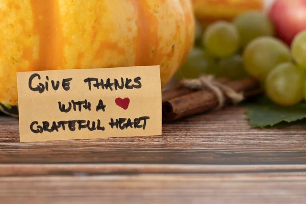 Give thanks with a grateful heart, a handwritten text on a vintage card with various autumn fruit in the background. A close-up. Christian thanksgiving, gratitude, and praise to God for all blessings.