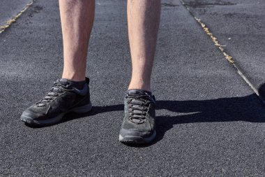 The legs of a man in black sneakers. Black and gray asphalt background. The concept of running and walking. Legs of young man in black sneakers. 