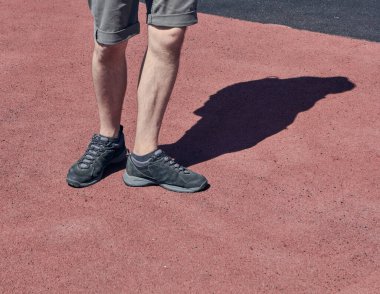 Kısa şortlu ve siyah ayakkabılı bir adamın bacakları. Kırmızı ve Brownnasphalt arka planı. Koşma ve yürüme kavramı. Siyah ayakkabılı genç adamın bacakları..